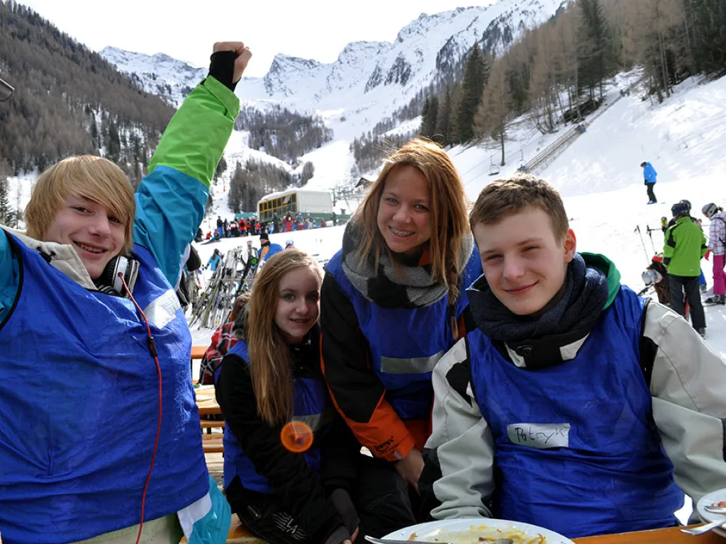 Vier Jugendliche posieren vor der verschneiten Bergkulisse.